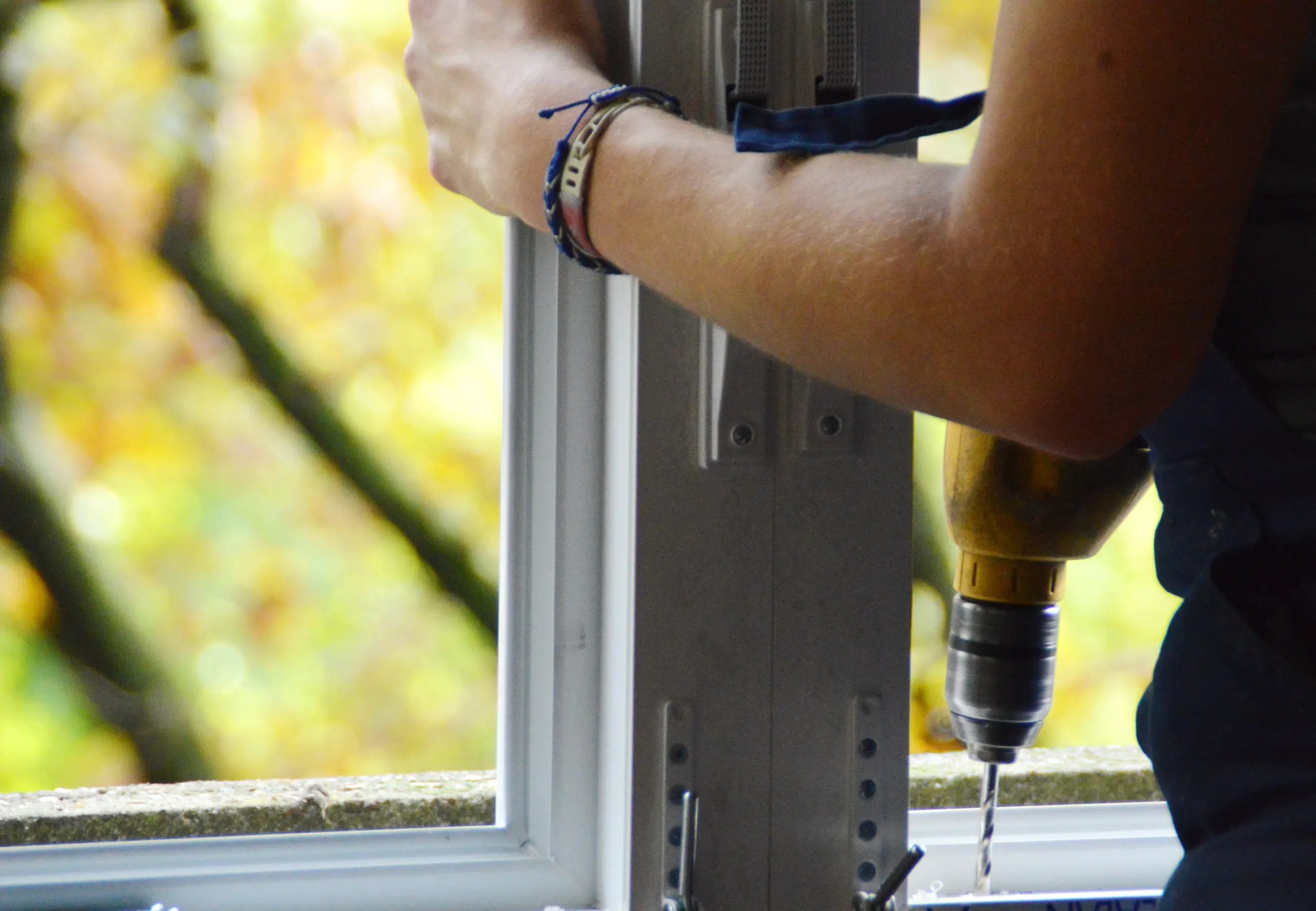Montaż okien - pracownik dokręca aluminiową ramę okna wiertarką